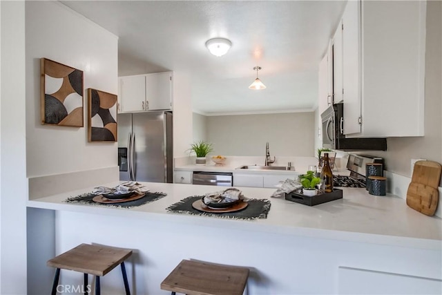 kitchen with appliances with stainless steel finishes, a peninsula, a sink, white cabinetry, and ornamental molding