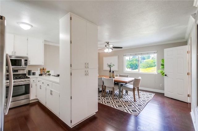 kitchen with appliances with stainless steel finishes, dark wood finished floors, ceiling fan, white cabinetry, and ornamental molding
