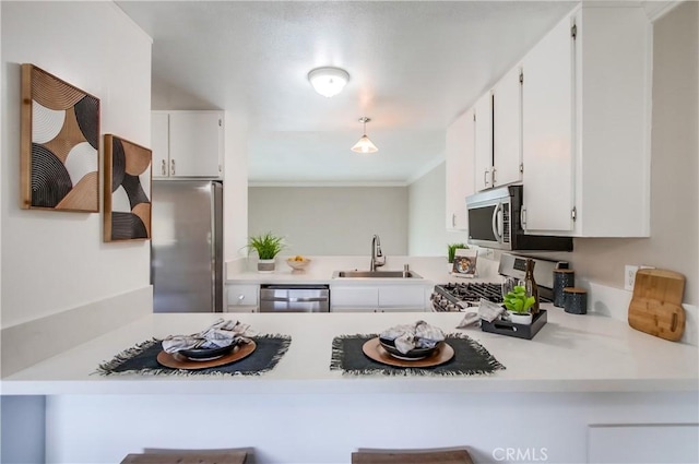 kitchen featuring a sink, appliances with stainless steel finishes, white cabinetry, ornamental molding, and a peninsula