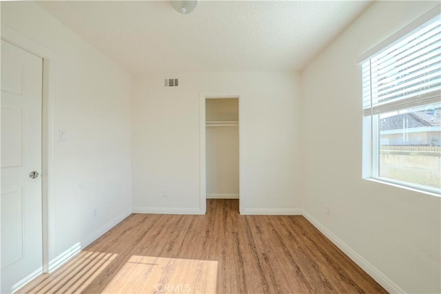 1517 W Romneya Dr, Anaheim, CA 92801 - unfurnished bedroom with light wood-style flooring, a walk in closet, a closet, baseboards, and a textured ceiling