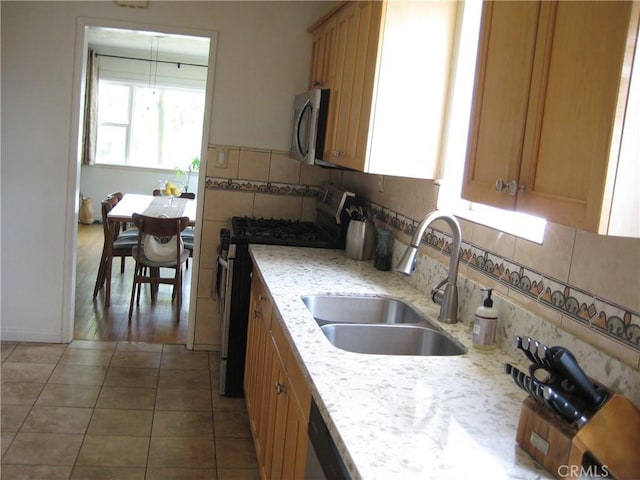 kitchen with stainless steel appliances, a sink, tile patterned floors, backsplash, and light stone countertops
