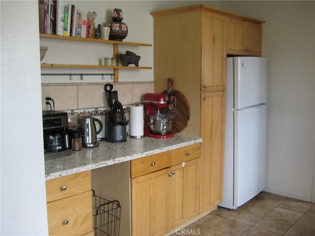 kitchen featuring freestanding refrigerator, backsplash, light tile patterned floors, light stone counters, and open shelves