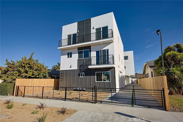 2402 S Cochran Ave, Los Angeles, CA 90016 - contemporary home featuring a balcony, a fenced front yard, a gate, board and batten siding, and stucco siding