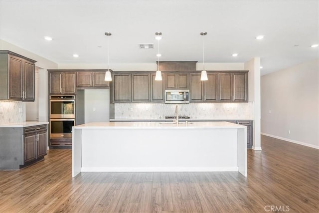 34428 Burnt Pine Rd, Murrieta, CA 92563 - kitchen featuring appliances with stainless steel finishes, backsplash, an island with sink, wood finished floors, and recessed lighting