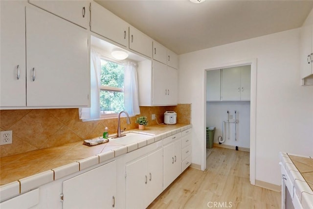 2234 Perkins Ave, Oroville, CA 95966 - kitchen featuring a sink, light wood finished floors, white cabinetry, tasteful backsplash, and tile counters