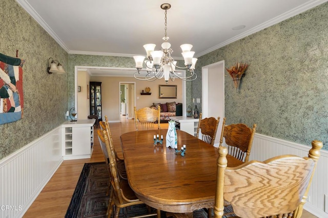 dining room featuring wood finished floors, a chandelier, wainscoting, crown molding, and wallpapered walls