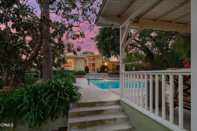 pool at dusk with an outdoor pool and a patio