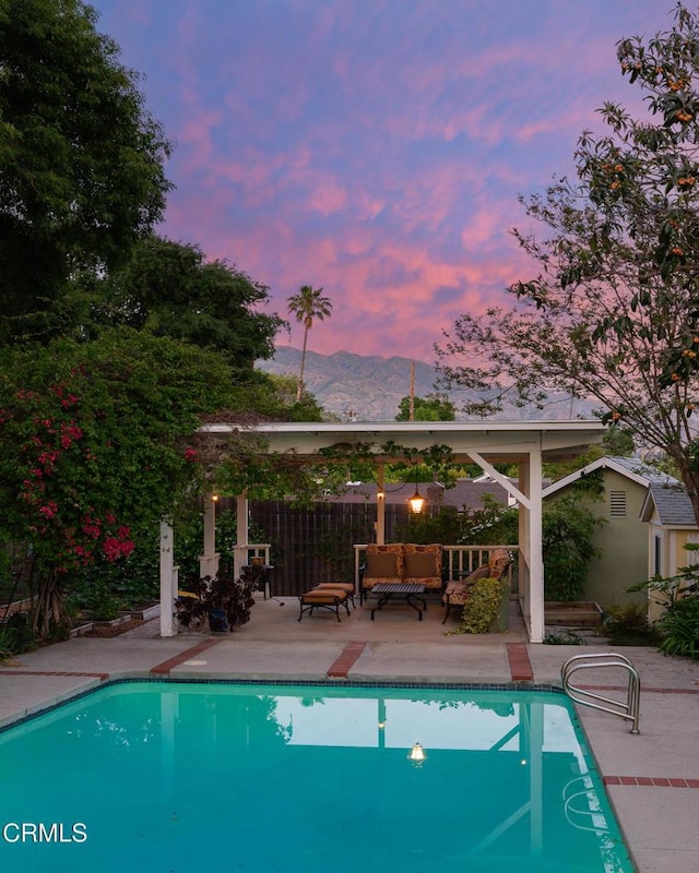 pool at dusk featuring an outdoor pool, fence, a patio, a mountain view, and outdoor lounge area
