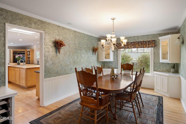 dining room featuring a chandelier, light wood finished floors, wallpapered walls, and crown molding