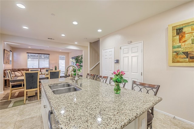 kitchen with a sink, a kitchen bar, a center island with sink, white cabinetry, and recessed lighting