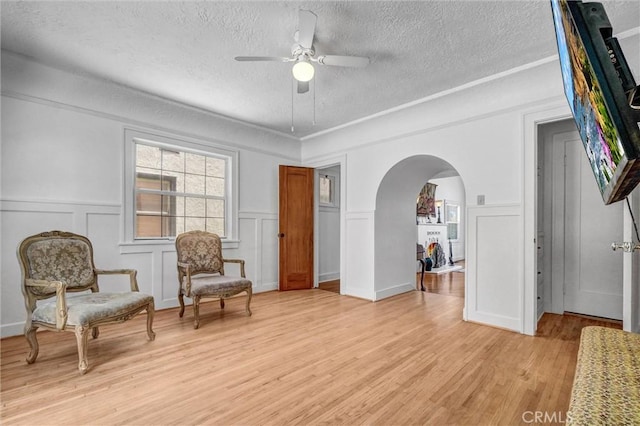 521 W Whiting Ave, Fullerton, CA 92832 - living area featuring a textured ceiling, a decorative wall, arched walkways, a ceiling fan, and light wood-type flooring