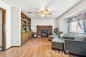 living area featuring a ceiling fan, wood finished floors, and a brick fireplace