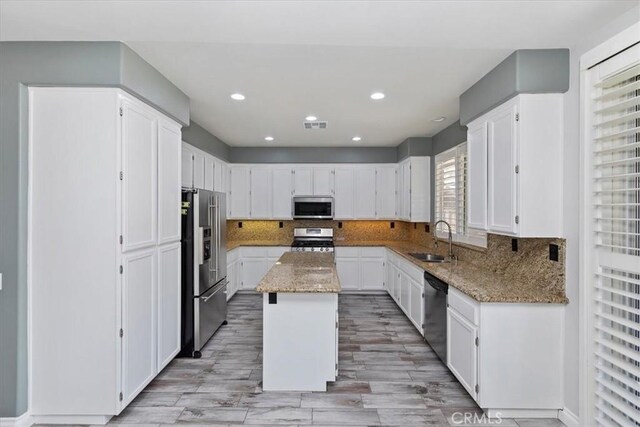 8433 Lindenhurst St, Riverside, CA 92508 - kitchen featuring appliances with stainless steel finishes, white cabinetry, light stone countertops, a center island, and backsplash