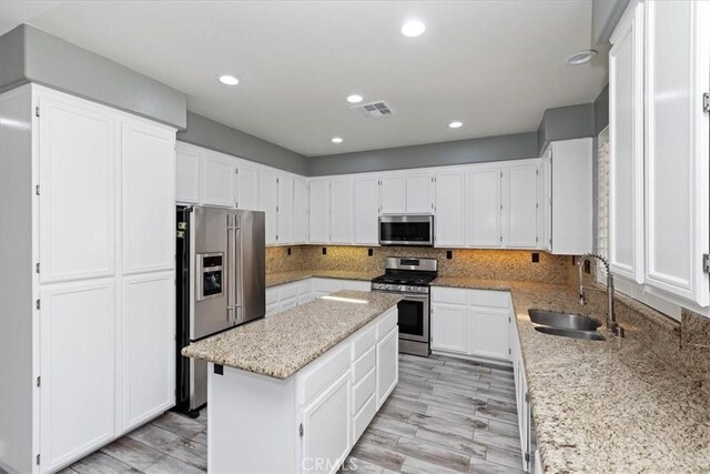8433 Lindenhurst St, Riverside, CA 92508 - kitchen featuring appliances with stainless steel finishes, a kitchen island, light stone counters, white cabinetry, and decorative backsplash