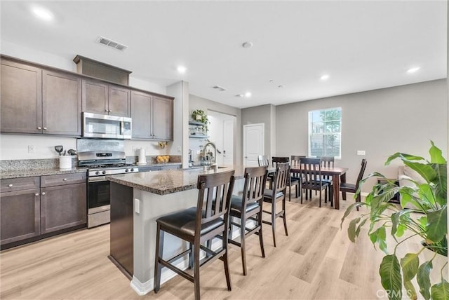 16548 Monteviejo St, Fontana, CA 92336 - kitchen with appliances with stainless steel finishes, a kitchen breakfast bar, dark brown cabinets, a sink, and light wood finished floors