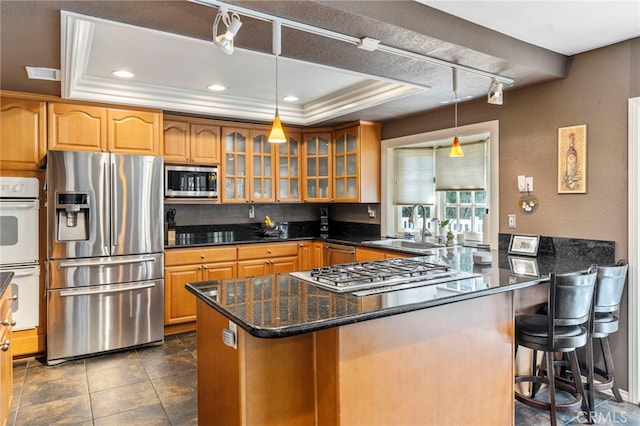 kitchen featuring stainless steel appliances, a sink, a raised ceiling, glass insert cabinets, and a peninsula