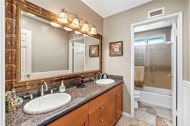 full bathroom featuring toilet, double vanity, stone tile flooring, and shower / bath combination