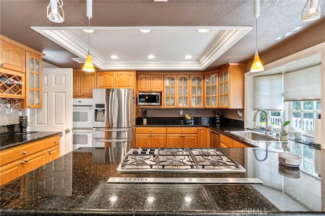 kitchen with appliances with stainless steel finishes, ornamental molding, a raised ceiling, a sink, and brown cabinetry