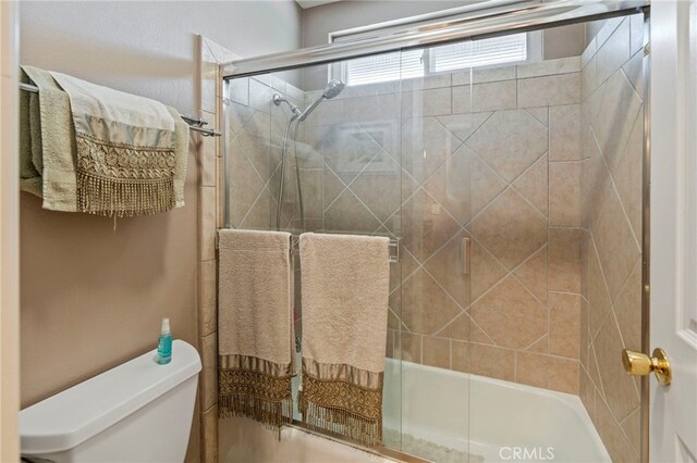 full bath featuring toilet and shower / bath combination with glass door
