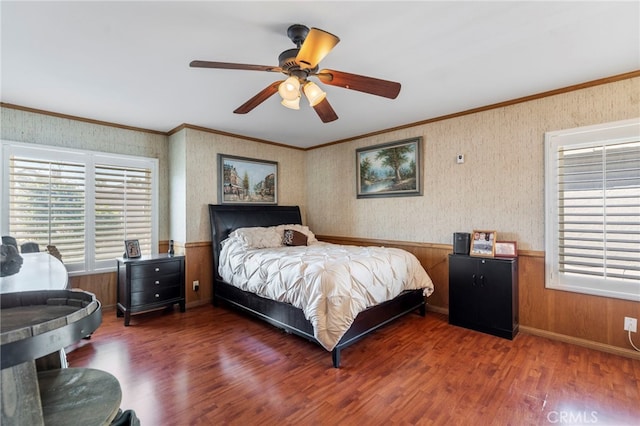 bedroom featuring multiple windows, crown molding, wood finished floors, a ceiling fan, and wallpapered walls