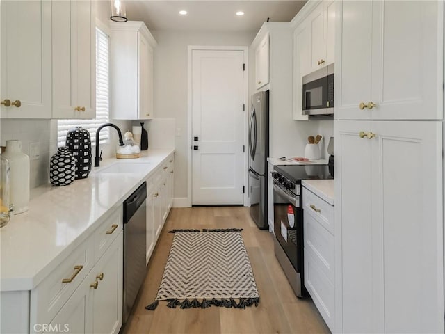 613 E Walnut Ave, Monrovia, CA 91016 - kitchen featuring appliances with stainless steel finishes, a sink, light wood-style floors, white cabinetry, and backsplash