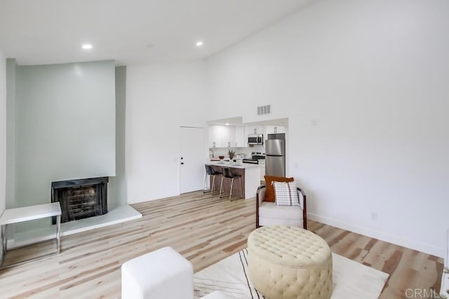 living room with light wood-style flooring, a fireplace, high vaulted ceiling, and recessed lighting