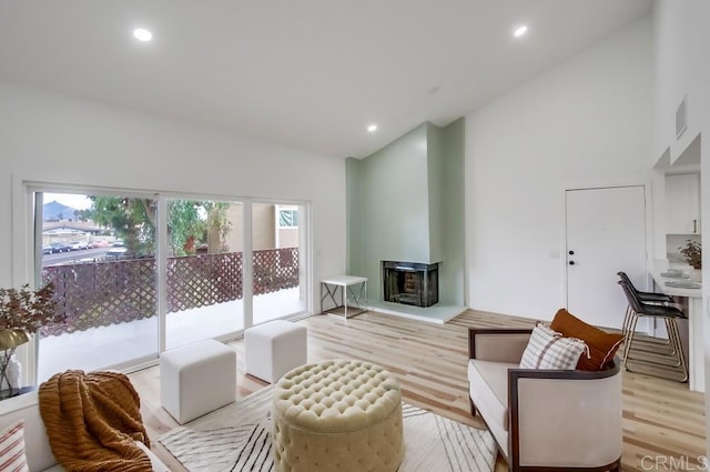 living room with plenty of natural light, light wood finished floors, recessed lighting, a multi sided fireplace, and high vaulted ceiling