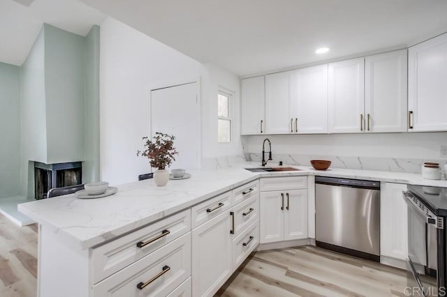 kitchen featuring stainless steel dishwasher, a sink, light wood-type flooring, a peninsula, and white cabinets