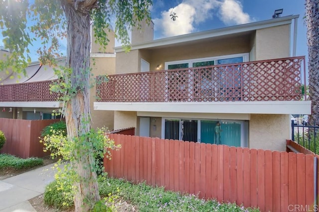 view of front of property featuring a balcony, stucco siding, and fence