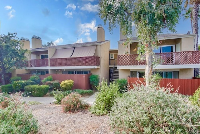 rear view of property with a chimney, stucco siding, and fence