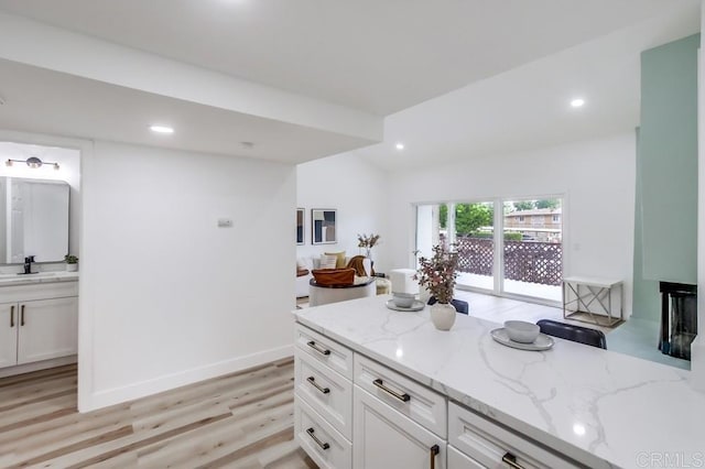 kitchen featuring light wood finished floors, light stone counters, white cabinetry, recessed lighting, and a sink