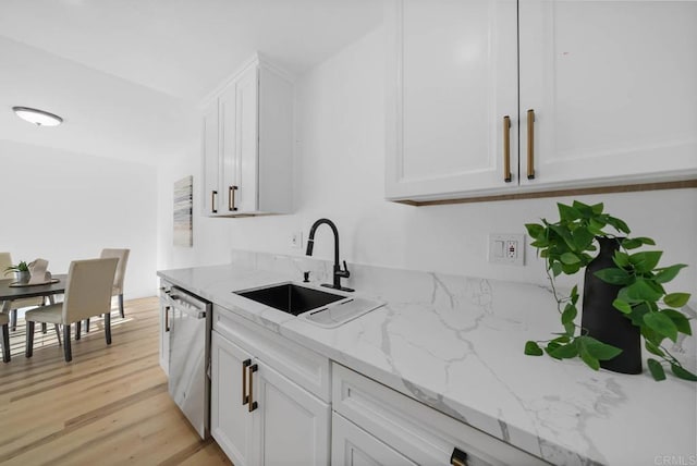 kitchen featuring stainless steel dishwasher, a sink, white cabinetry, light stone countertops, and light wood-type flooring