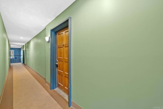 hall featuring carpet flooring, baseboards, and a textured ceiling