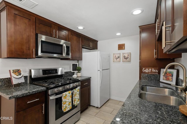 kitchen with appliances with stainless steel finishes, a sink, light tile patterned flooring, recessed lighting, and dark stone counters