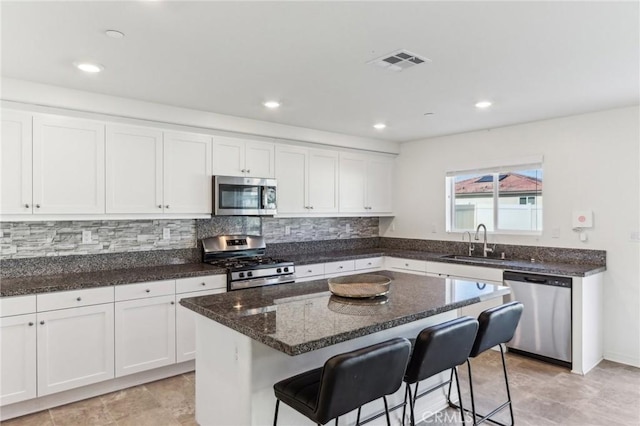 29586 Bisbee Ct, Winchester, CA 92596 - kitchen featuring appliances with stainless steel finishes, a sink, white cabinets, a kitchen bar, and dark stone countertops