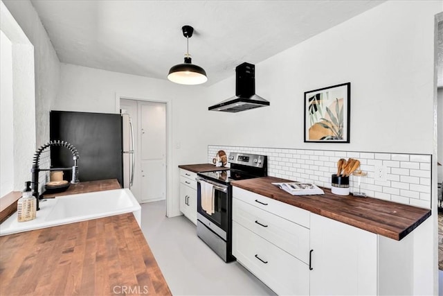 kitchen featuring butcher block counters, appliances with stainless steel finishes, wall chimney exhaust hood, backsplash, and white cabinetry