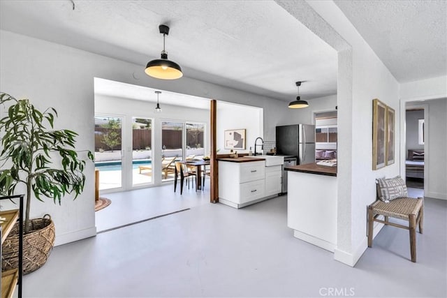 kitchen featuring stainless steel appliances, a textured ceiling, concrete flooring, white cabinets, and hanging light fixtures
