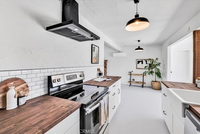 kitchen featuring appliances with stainless steel finishes, island range hood, butcher block counters, a wall mounted air conditioner, and backsplash