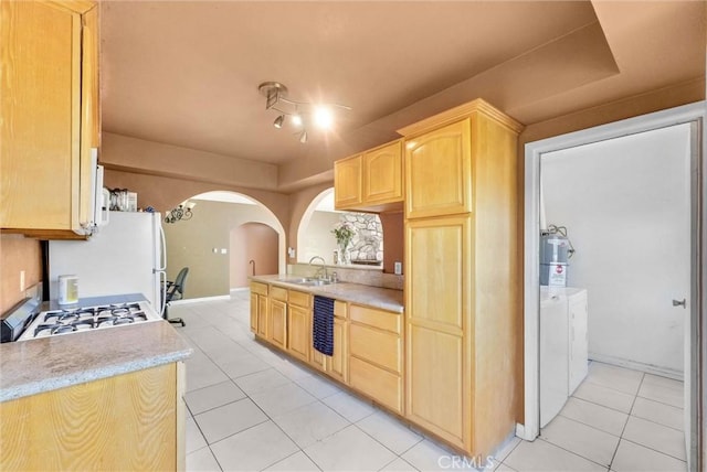 kitchen featuring independent washer and dryer, light brown cabinetry, arched walkways, a sink, and light countertops
