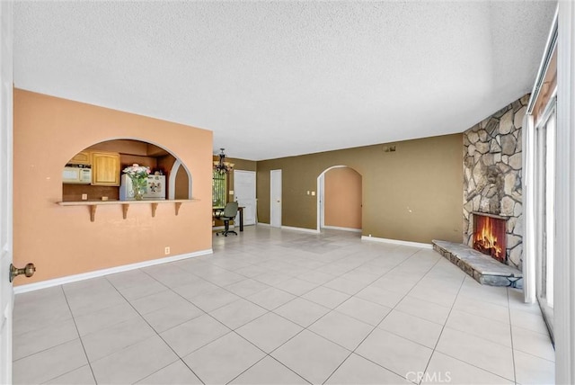 unfurnished living room featuring a textured ceiling, a fireplace, light tile patterned floors, arched walkways, and baseboards