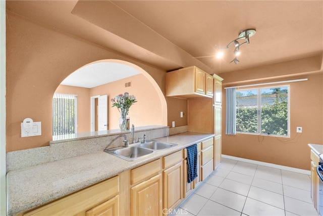 kitchen featuring a sink, light brown cabinets, light tile patterned floors, baseboards, and arched walkways