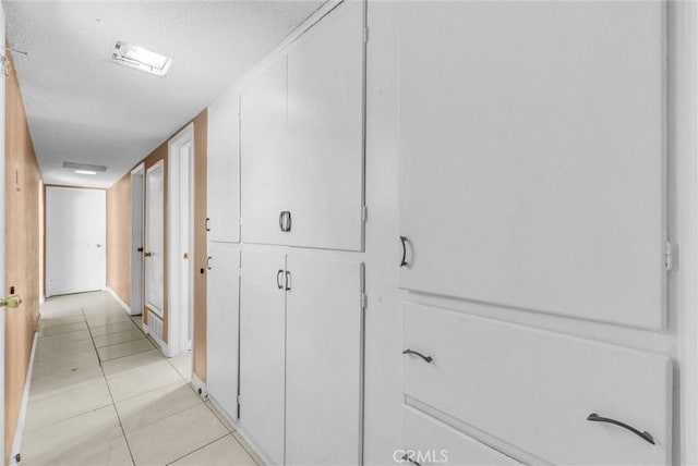 hall featuring light tile patterned floors, a textured ceiling, and baseboards