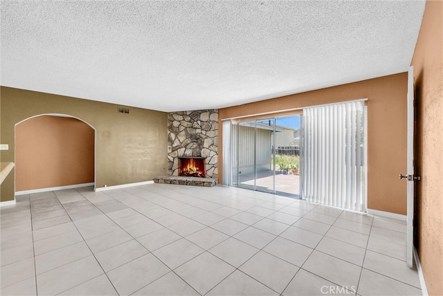 unfurnished living room featuring a textured ceiling, light tile patterned flooring, a stone fireplace, and arched walkways