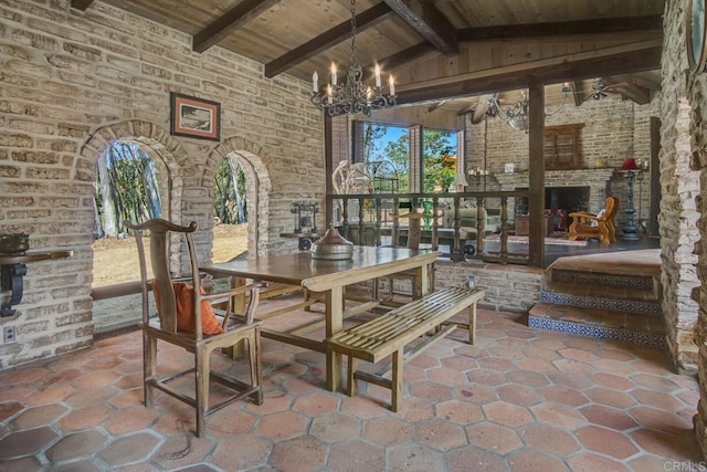 15390 Las Planideras, Rancho Santa Fe, CA 92067 - dining area with wooden ceiling, brick wall, a chandelier, stone tile flooring, and an outdoor fireplace