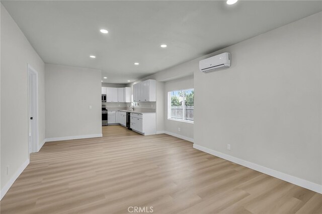 970 E 6th St, Pomona, CA 91766 - unfurnished living room with a wall mounted air conditioner, recessed lighting, light wood-type flooring, baseboards, and a sink