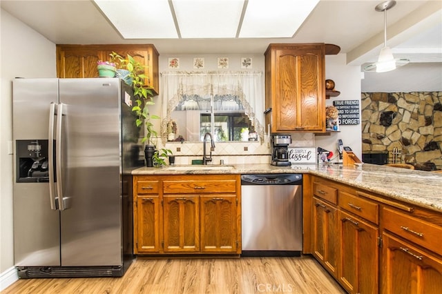 kitchen with stainless steel appliances, a sink, backsplash, brown cabinets, and light stone countertops