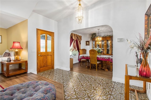 entryway featuring arched walkways, a chandelier, wood finished floors, baseboards, and vaulted ceiling
