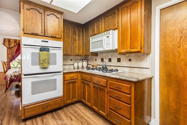 kitchen with white appliances, light wood finished floors, decorative backsplash, and brown cabinetry