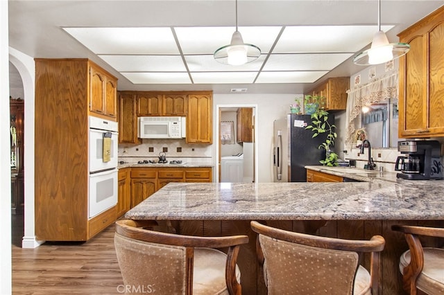 kitchen featuring white appliances, washer / dryer, a peninsula, light wood-style floors, and a breakfast bar area