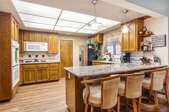 kitchen featuring white appliances, a peninsula, backsplash, and light wood-type flooring
